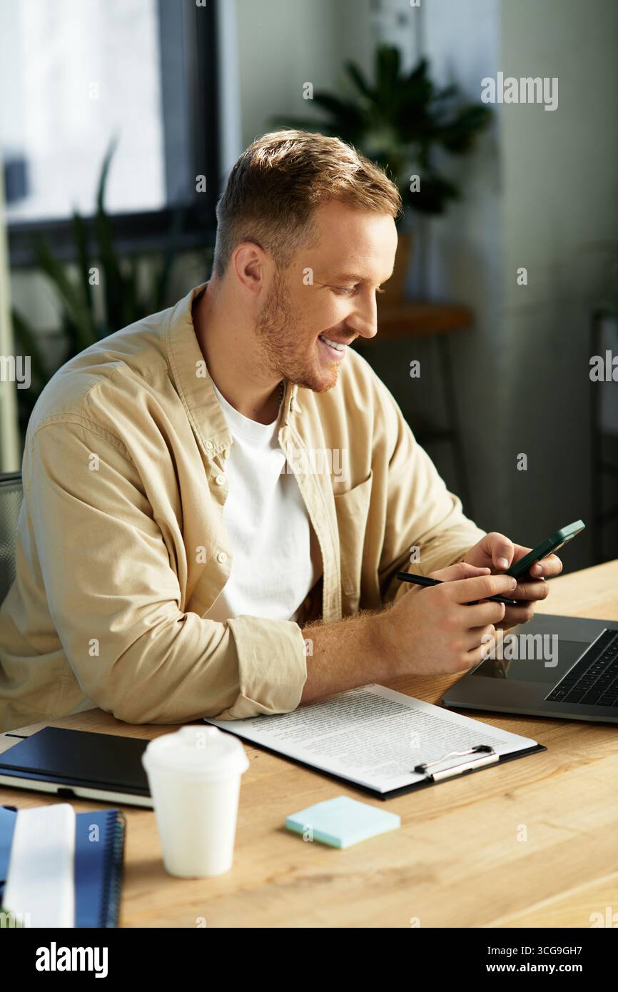 A young businessman smiles while using his phone, immersed in his work at a stylish office. Stock Photo