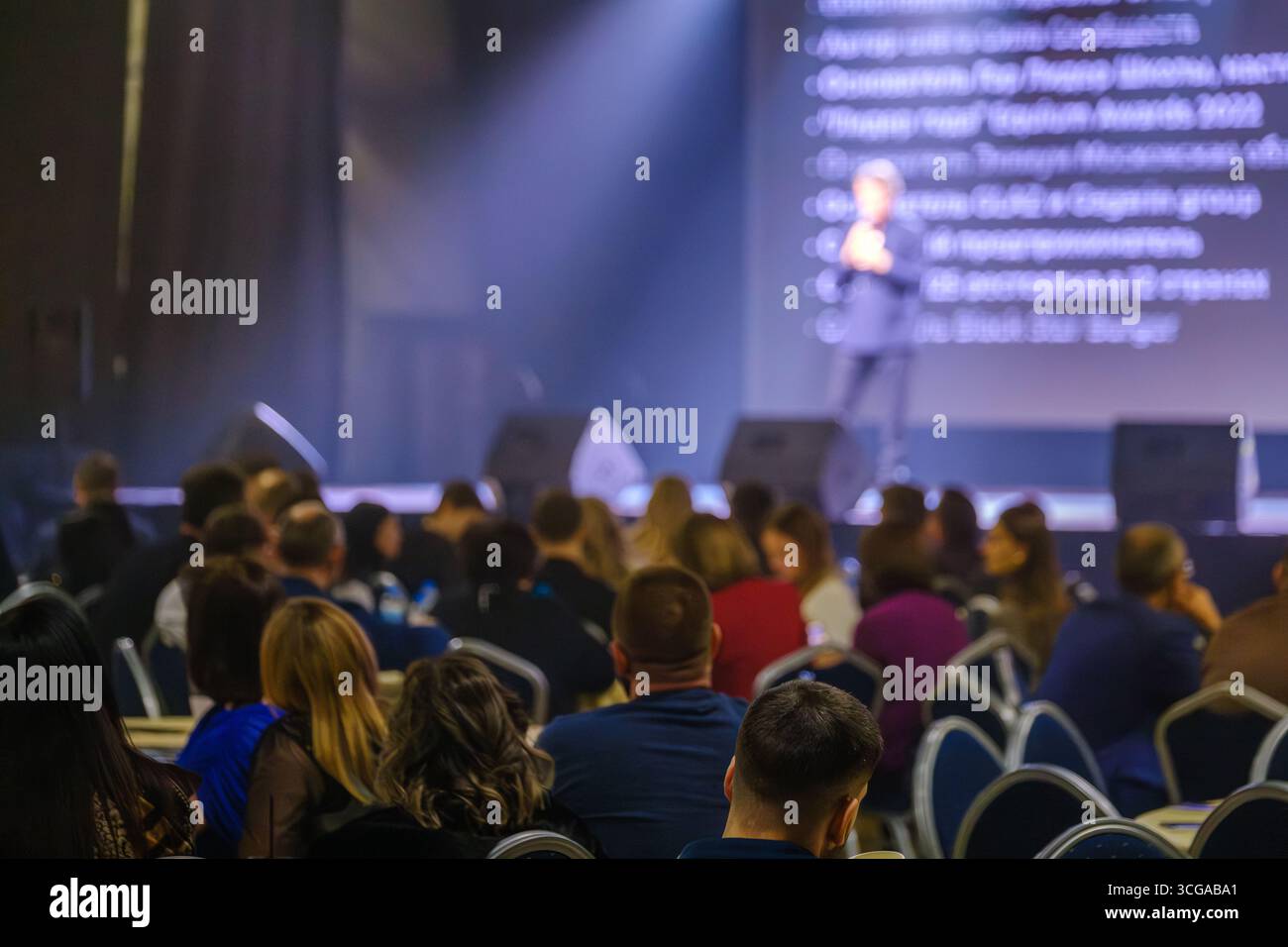 Business professionals attending a conference, listening to presentations on a well-lit stage Stock Photo