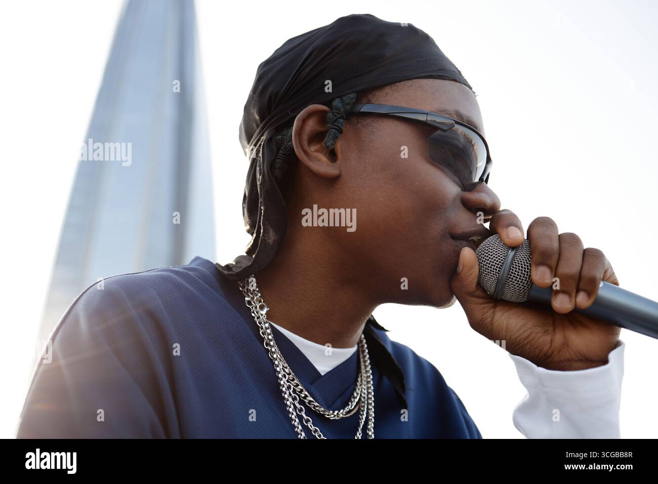 Young Black Man Singing into Microphone Outdoors Wearing Sunglasses and Chains Stock Photo