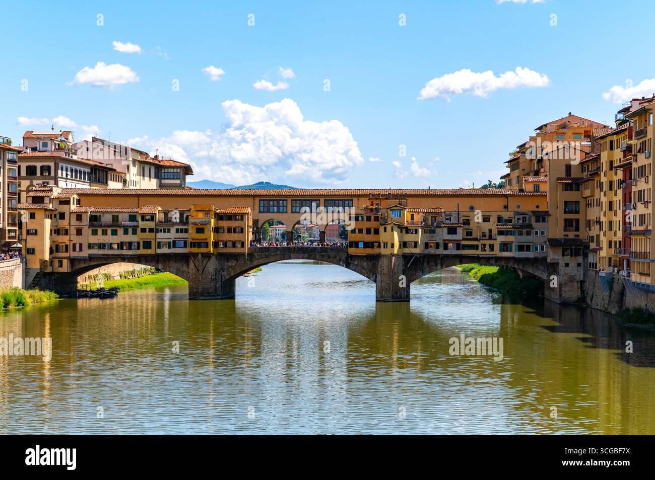 Historic Ponte Vecchio bridge in Florence, Italy, spans the Arno River with charming shop-lined architecture under a clear blue sky. Stock Photo