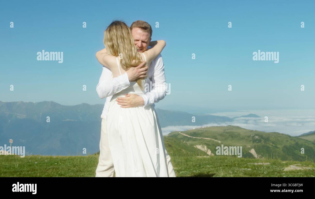 Dance on a grassy mountain peak under clear blue sky, celebrating love and freedom in nature. Stock Photo