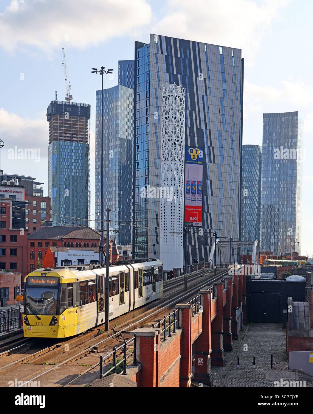Yellow Manchester Metrolink tram operates through Castlefield in Manchester city centre, with modern high-rise apartment towers and office buildings Stock Photo