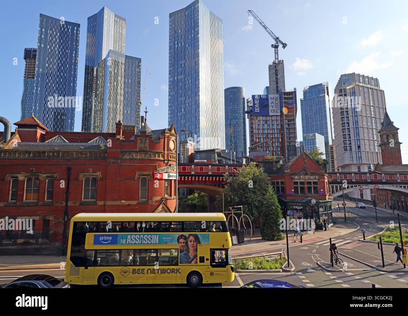 A yellow Bee Network bus travels through Deansgate in Manchester city centre, passing Deansgate Station (formerly Knott Mill), with newly built blocks Stock Photo