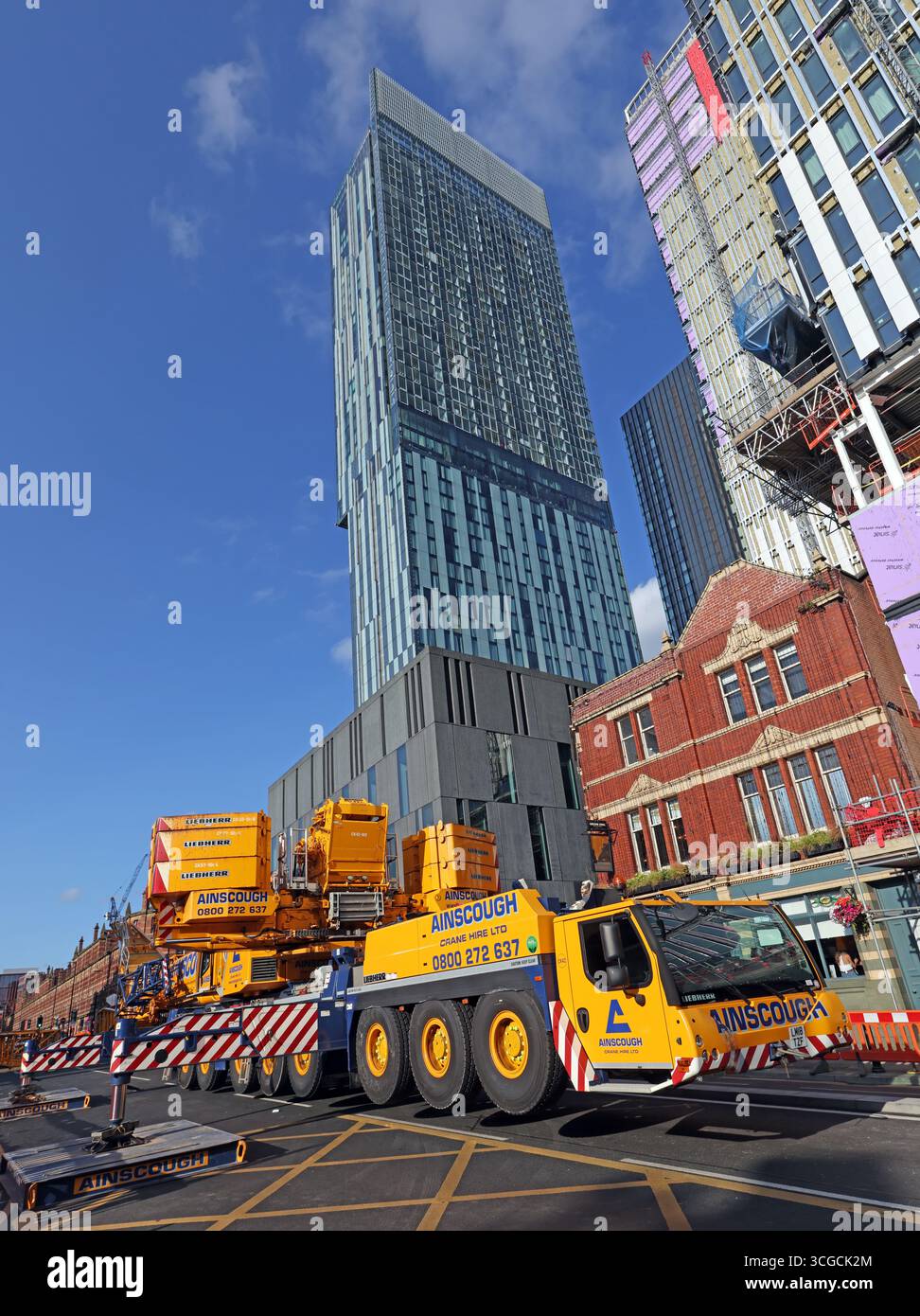 A large mobile crane operated by Ainscough closes Deansgate in Manchester city centre during lifting operations, with the Beetham Tower and Hilton Stock Photo