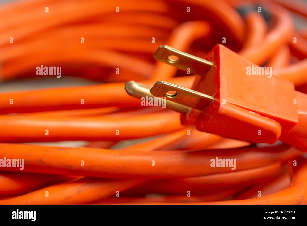 A closeup view of the prongs on a plug of an orange extension cord. Stock Photo