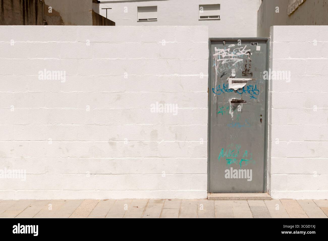 A white wall or wall ideal for graffiti or murals, with a metal gate. A wall for a construction project, on an empty lot, with a plain white wall. Stock Photo