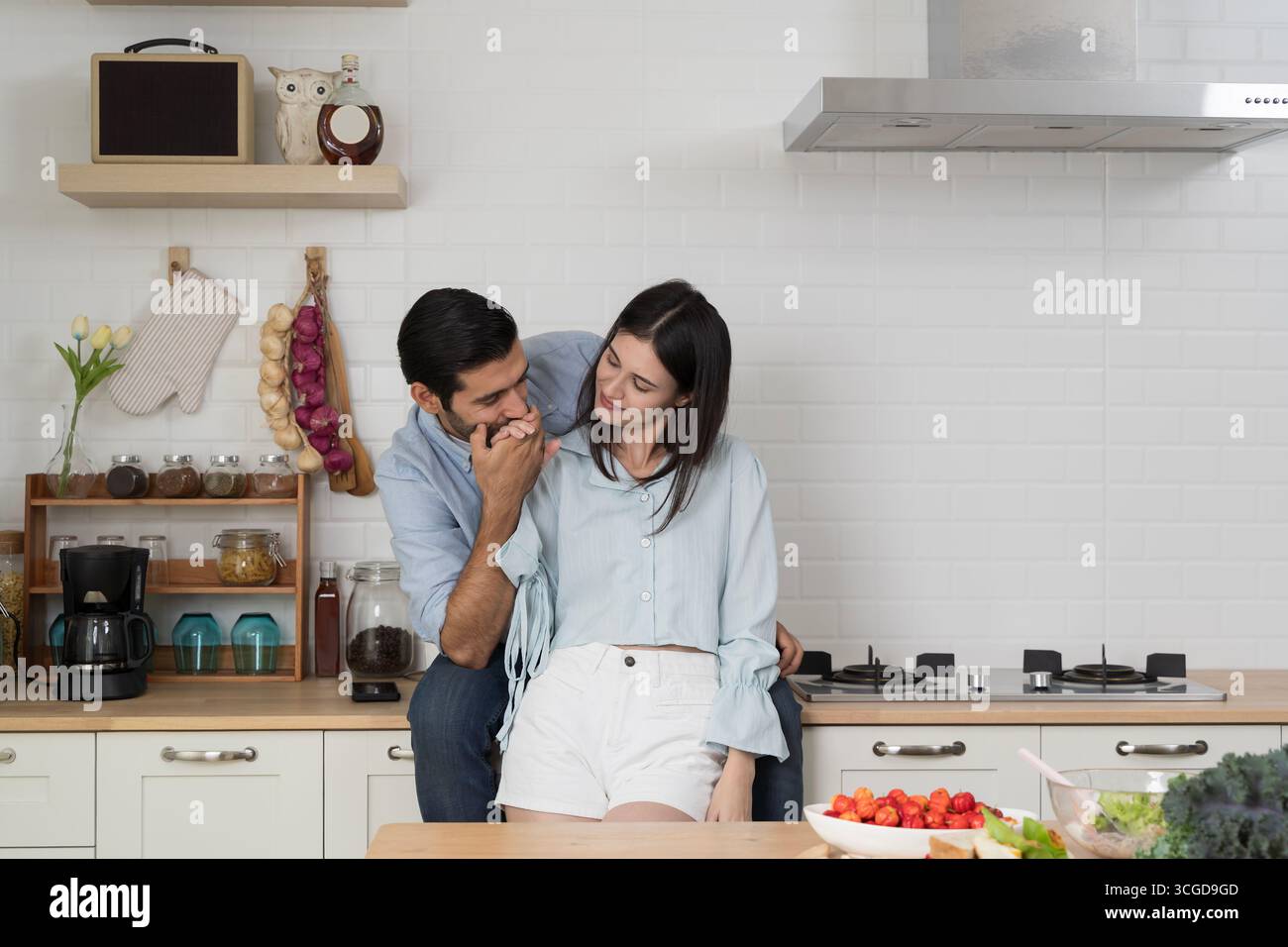 Young romantic couple in modern kitchen, man kissing woman’s hand with love and tenderness, representing romance, affection, wellness, family bonding, Stock Photo