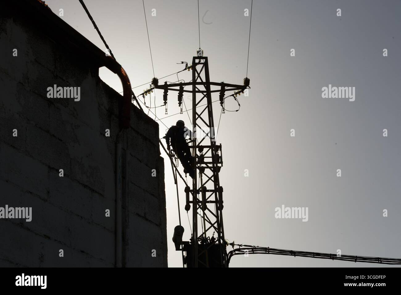 A workers silhouette stands out against a bright sky as they climb a power pole to perform essential maintenance tasks Stock Photo
