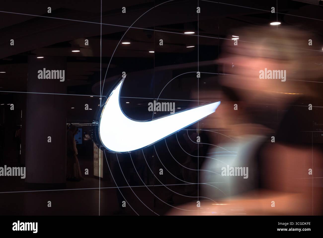 Bangkok, Thailand - August 23, 2025 : A pedestrian passes by a Nike, an American athletic equipment company, store with its logo displayed. Stock Photo