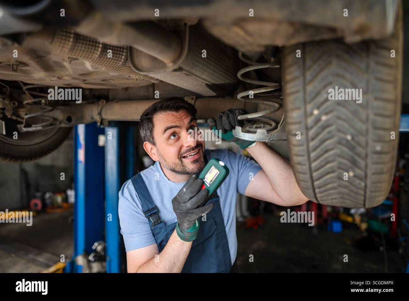 Professional mechanic inspecting car's undercarriage with flashlight in a repair shop Stock Photo