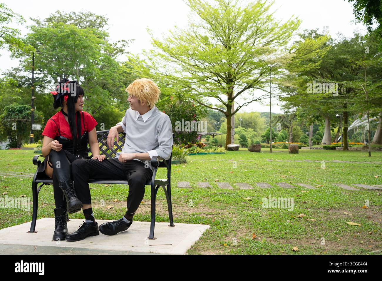 Two cosplayers are sitting on a bench in a park, enjoying conversation and portraying fictional characters Stock Photo