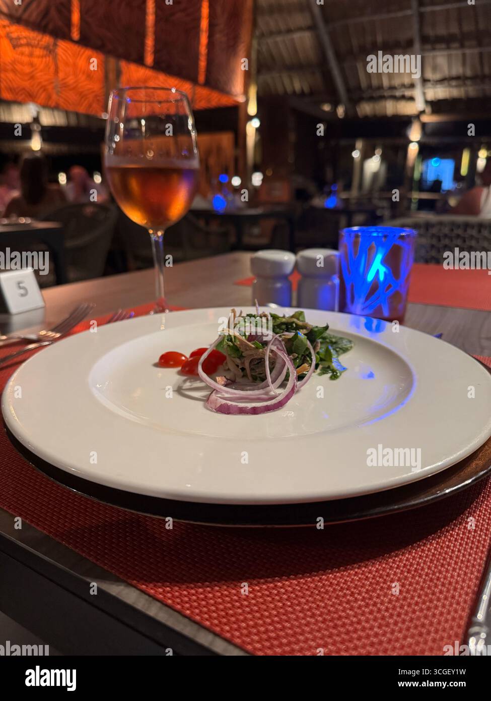 Fresh salad with onions and tomatoes served with wine glass on a dining table in Zanzibar, Tanzania, highlighting tropical gourmet cuisine and lifestyle - Smartphone Captured Stock Image