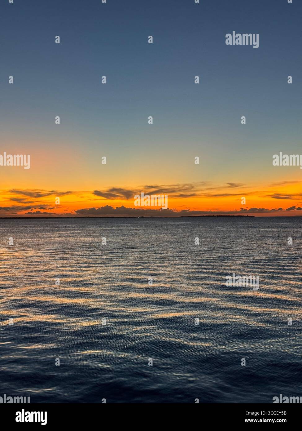 Brilliant orange sunset lights the horizon above calm ocean waters in Zanzibar, Tanzania, creating a peaceful tropical seascape and serene evening view - Smartphone Captured Stock Image