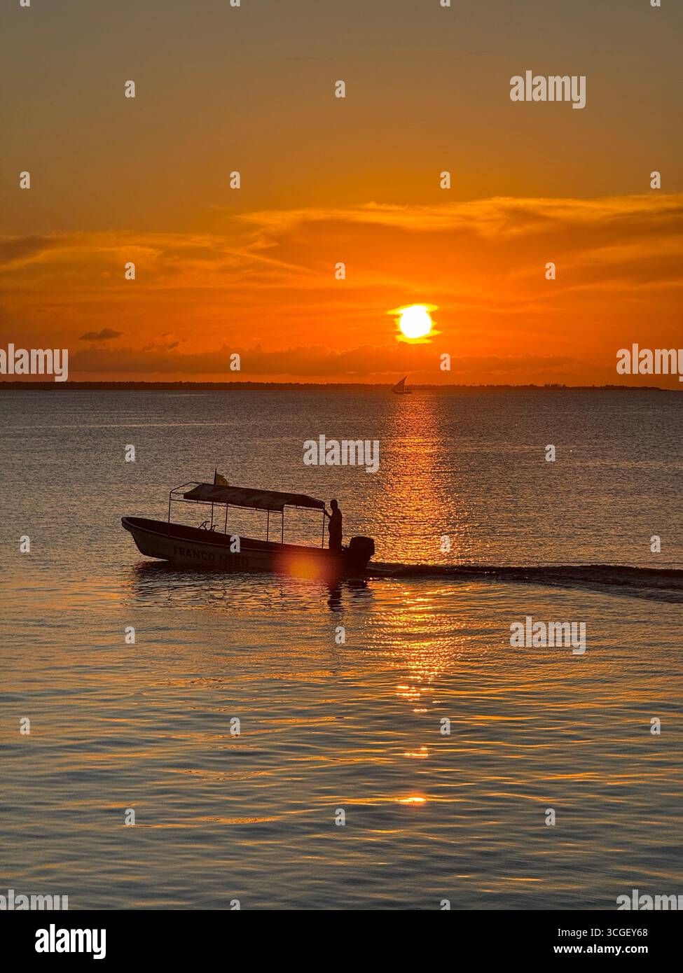 Small boat cruising on ocean waters during glowing golden sunset in Zanzibar, Tanzania, reflecting peaceful light and serene tropical coastal atmosphere - Smartphone Captured Stock Image