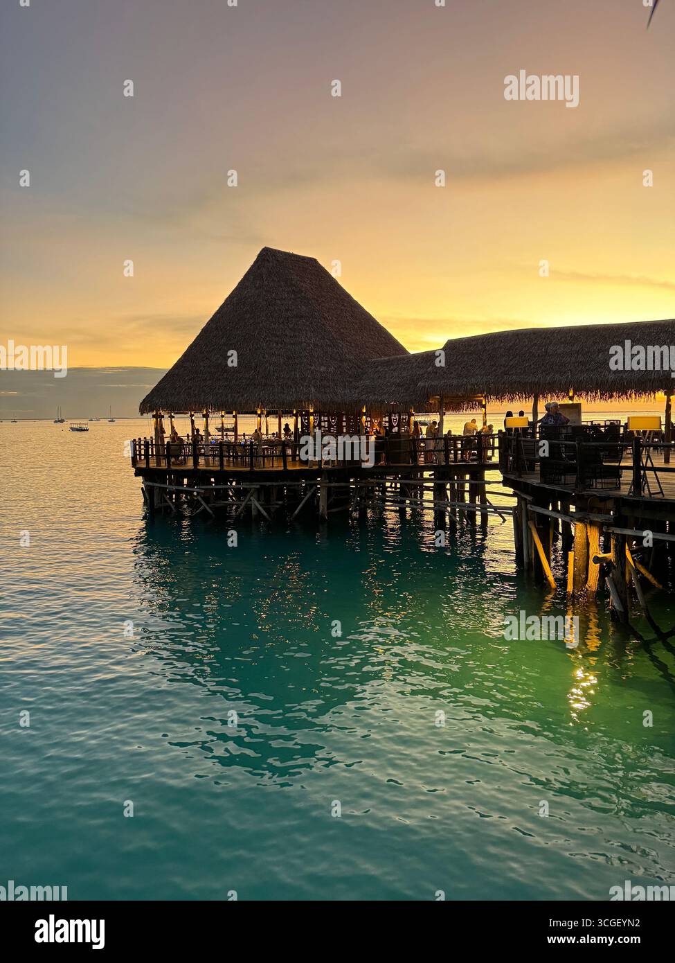Golden sunset view over an overwater lodge in Zanzibar, Tanzania, reflecting colors across turquoise ocean waters and creating a romantic travel moment - Smartphone Captured Stock Image