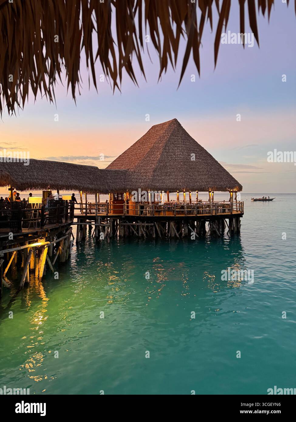 Thatched hut over turquoise ocean waters at golden sunset in Zanzibar, Tanzania, creating a serene tropical travel and resort atmosphere for visitors - Smartphone Captured Stock Image