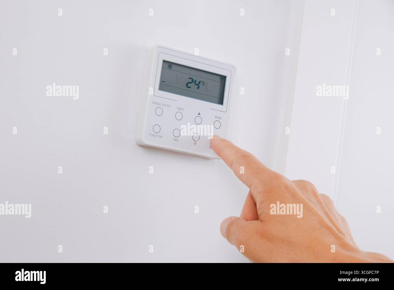 a man places his finger on the display of an air conditioning unit showing 24 degrees celsius in cooling mode, switching the system on or off to adjus Stock Photo