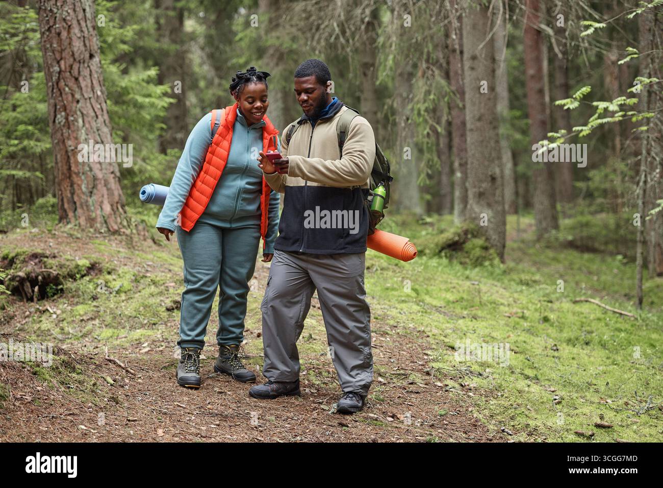 Young Black Couple Hiking in Forest Using Smartphone for Navigation Stock Photo