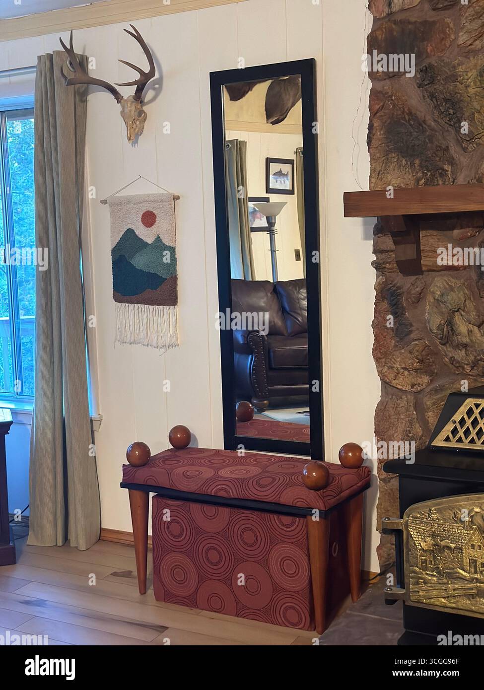 A rustic cabin-style interior featuring a stone fireplace, wall-mounted antlers, woven wall art, framed mirror, and patterned wooden bench - Smartphone Captured Stock Image