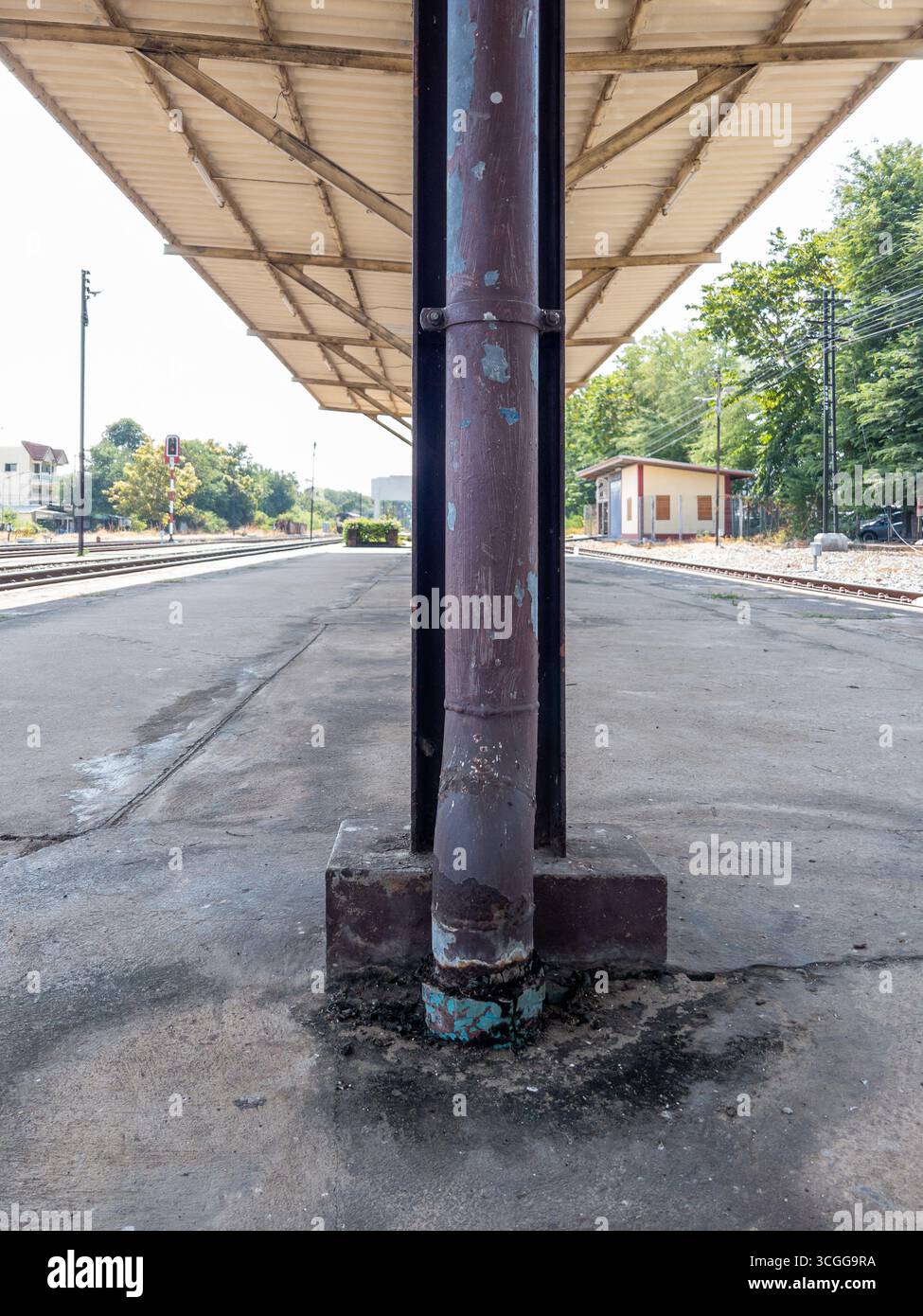 A rusty rain gutter on a column under the afternoon roof of a train station platform. Perfect for urban travel and infrastructure themes with tracks a Stock Photo