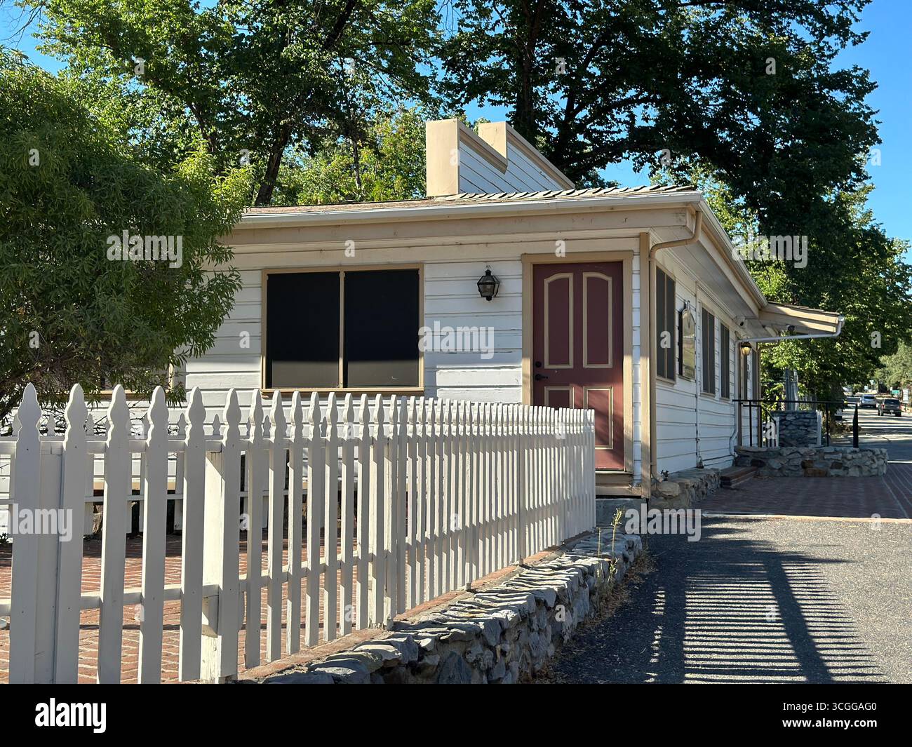 A traditional wooden house with a red front door and white picket fence, surrounded by trees in a small California town. - Smartphone Captured Stock Image