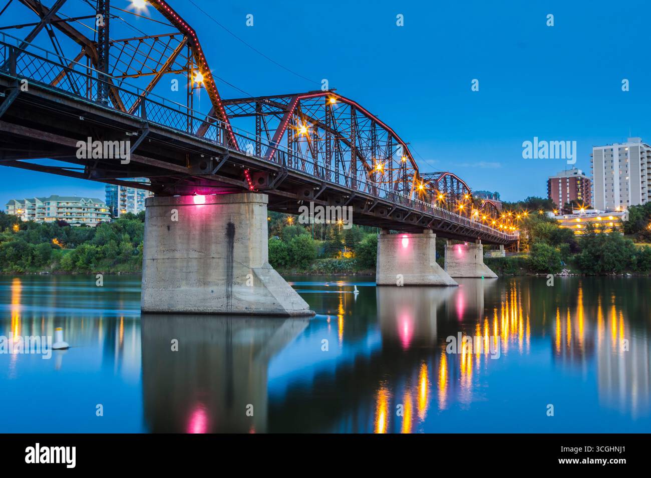 The Traffic Bridge illuminated after dark, casting reflections across the South Saskatchewan River in downtown Saskatoon. Stock Photo