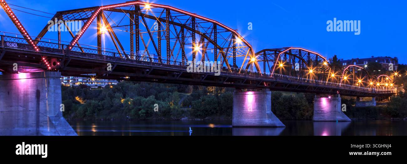The Traffic Bridge illuminated after dark, casting reflections across the South Saskatchewan River in downtown Saskatoon. Stock Photo