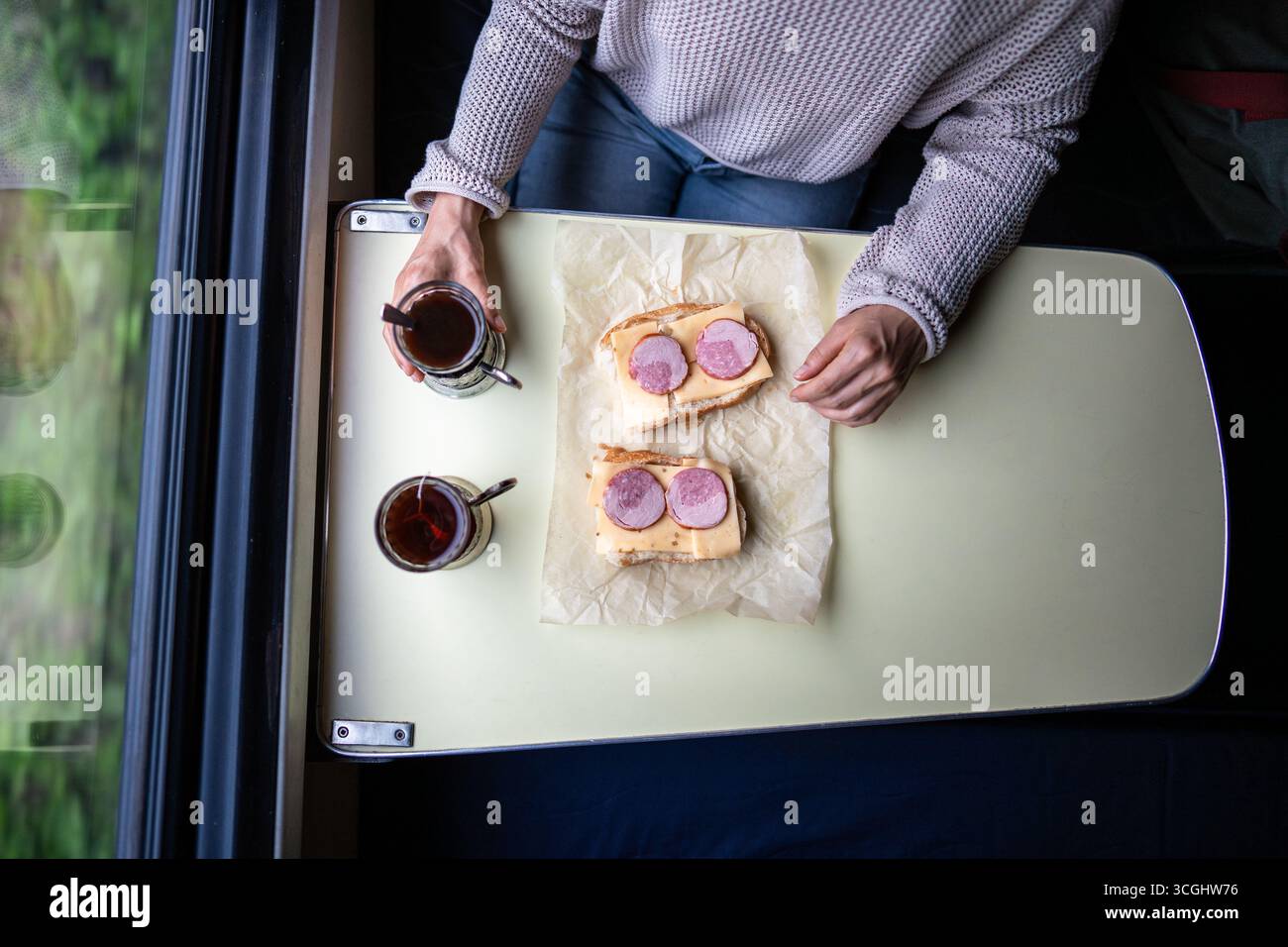 Train lunch, solo woman eating sandwich drinking tea waiting neighbor on travel commute journey Stock Photo