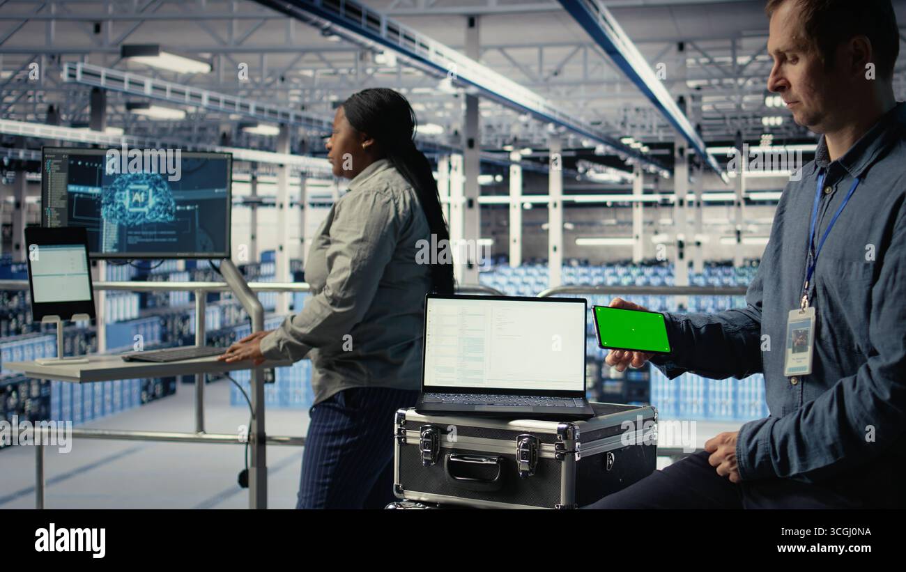 Data center worker uses isolated screen smartphone while deploying deep learning software. Server hub employee uses chroma key mobile phone while training AI systems with datasets, camera A Stock Photo