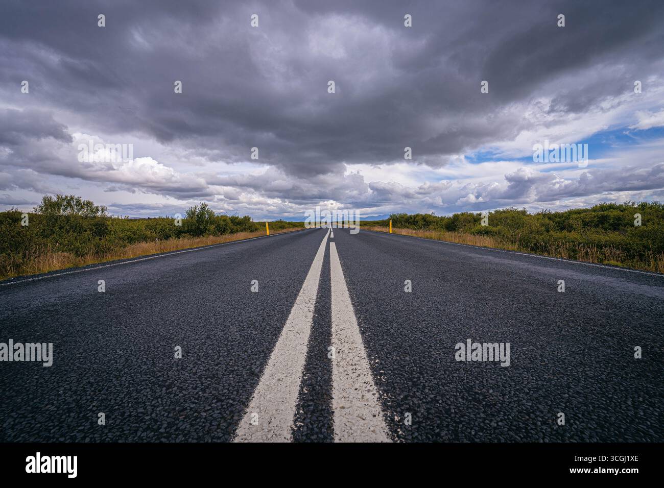 An endless Icelandic road stretches into the horizon beneath brooding storm clouds, a cinematic path through untamed wilderness and open skies Stock Photo
