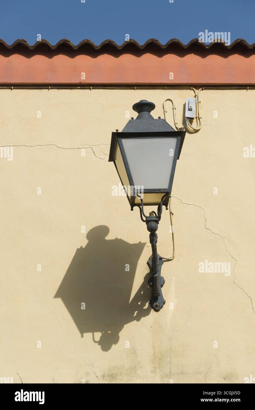 Street lamp placed on the facade of a school in the city of Huelva on a yellow wall and under a red tiled roof leaving a shadow on the wall Stock Photo
