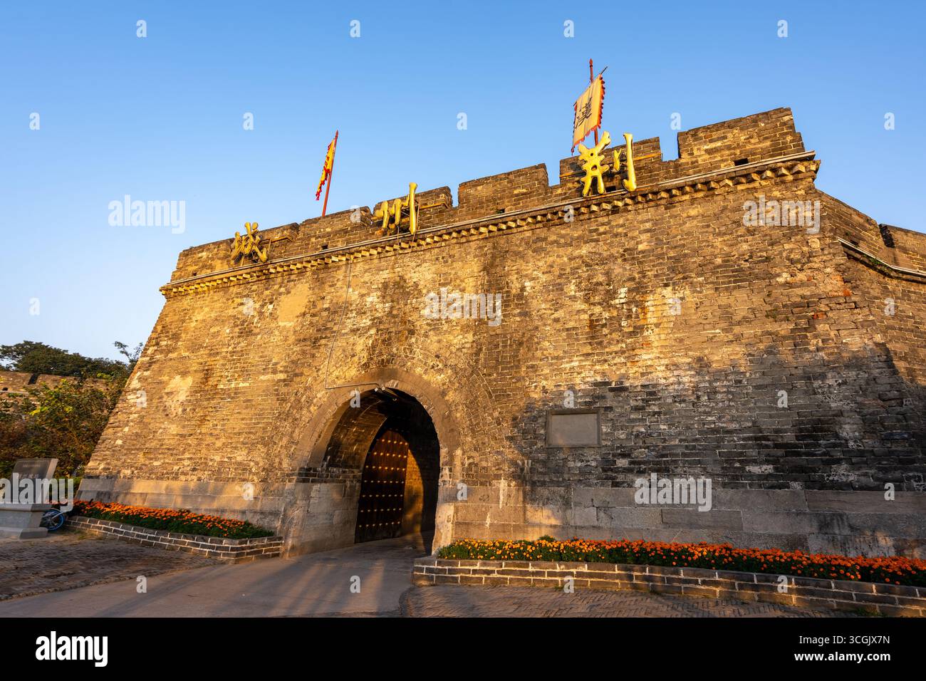 The ancient stone gate stands bathed in golden light, with flags flying ...