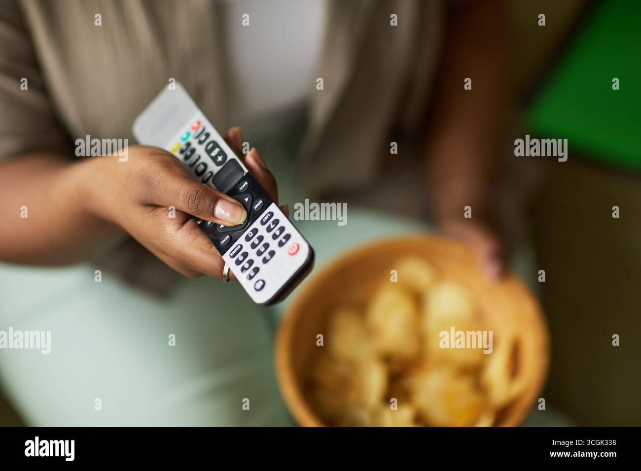 Black woman holding television remote control while sitting and eating ...