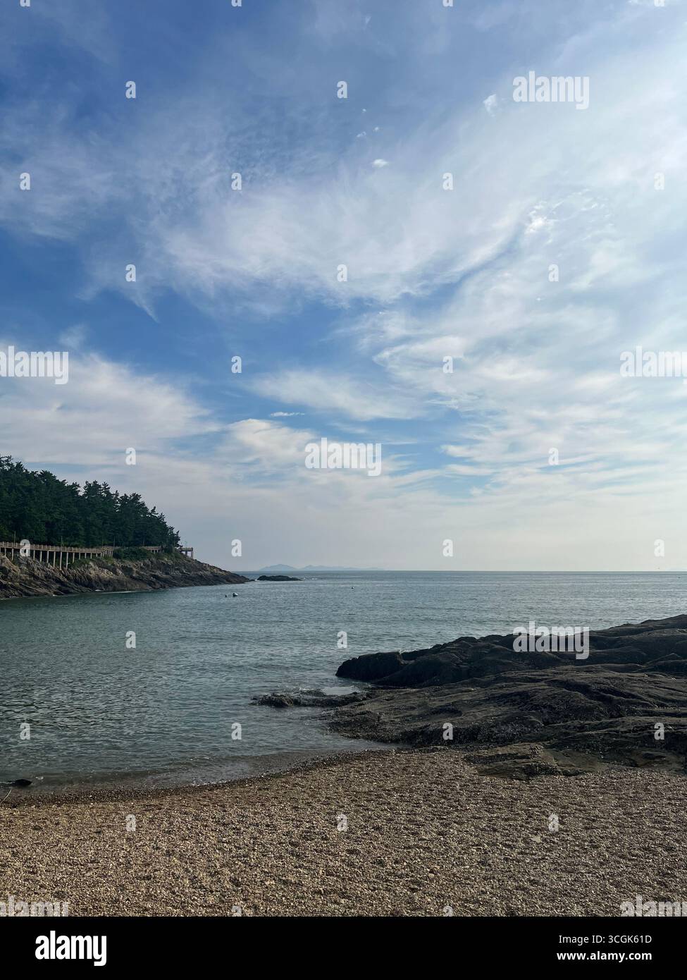 Quiet daytime view of Okdol Beach in South Korea, featuring calm sea, a coastal walkway, and a serene seaside landscape. - Smartphone Captured Stock Image