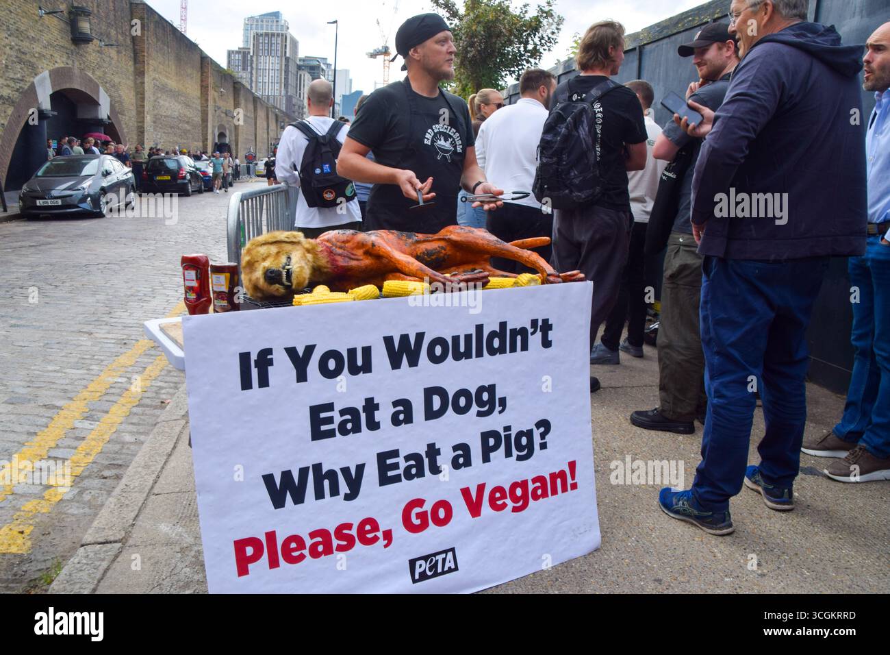 meat festival tobacco dock London, England, UK. 28th Aug, 2025. PETA activists stage a mock 'barbecue'  with a fake dog and a sign reading 'If you wouldn't eat a dog, why eat a  pig?' outside Meatopia