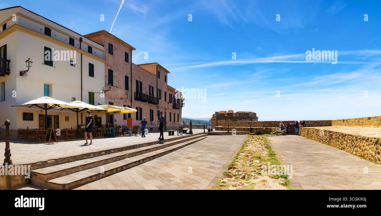 Algarve, Cerdeña, Italy - 05,04,2024: Seaside promenade in Alghero, Sardinia, with outdoor cafés, historic walls, blue sky, and people relaxing near t Stock Photo