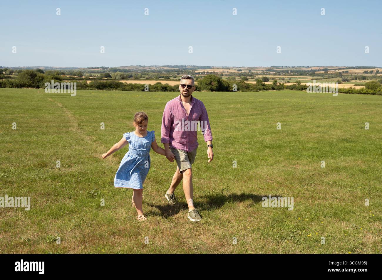 Father and daughter walking hand in hand through a field Stock Photo ...