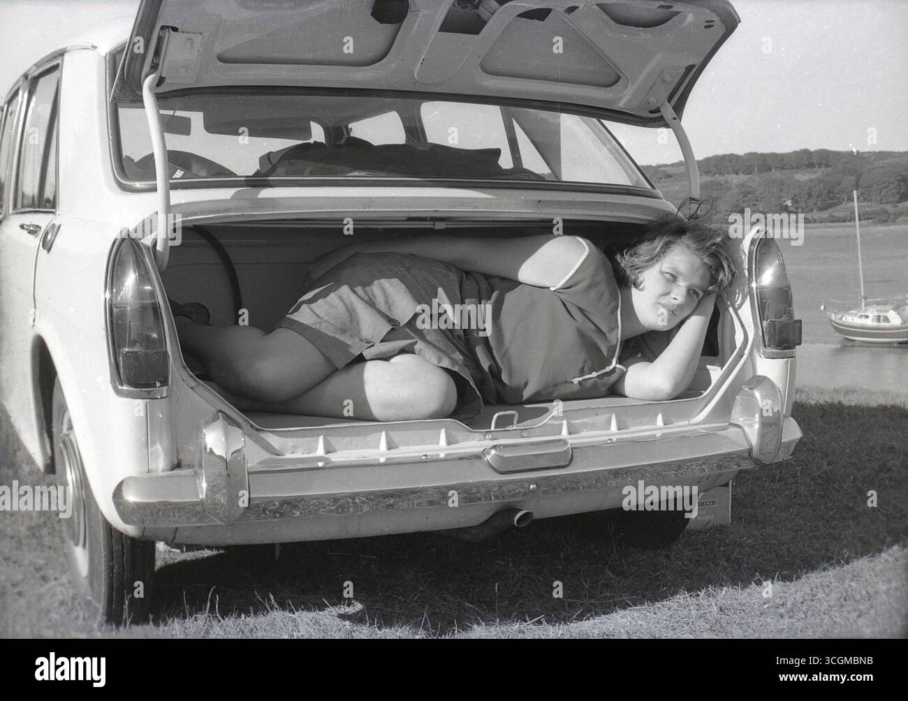 1960s, historical, a young woman lying in the boot of a BMC ADO16. As one does! Perhaps demonstrating how roomy it is. Made by the British Motor Corporation, the small family car was badged under a number of different names, the most popular being the Austin 1100 and Morris 1100, which was the name it was launched under in 1962. The Austin version was introduced the following year, made at BMC's Longbridge factory. A popular vehicle, from 1963 to 1966, it was best-selling car in Britain. Stock Photo