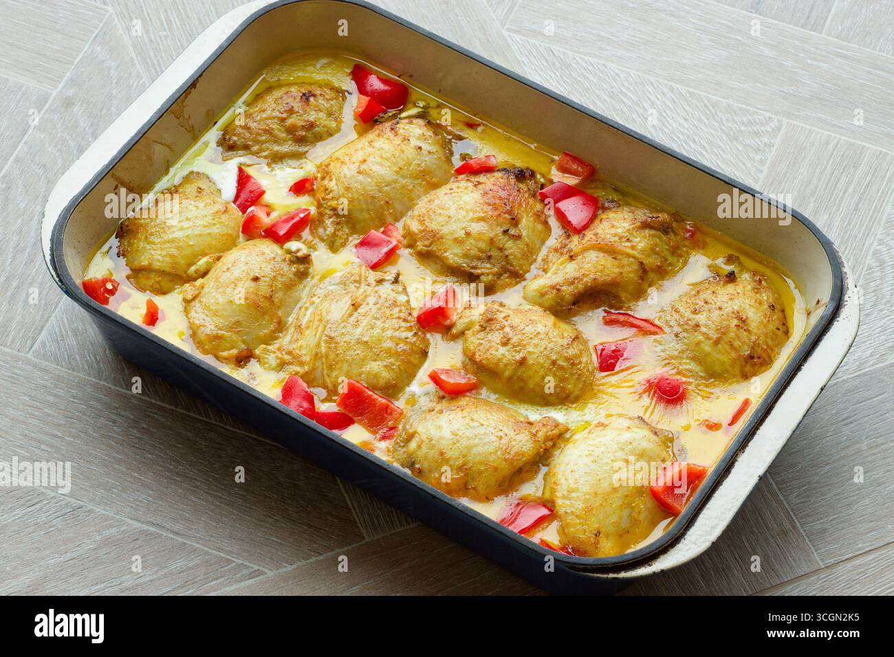A chicken thigh dish in a turmeric sauce with red peppers. Stock Photo