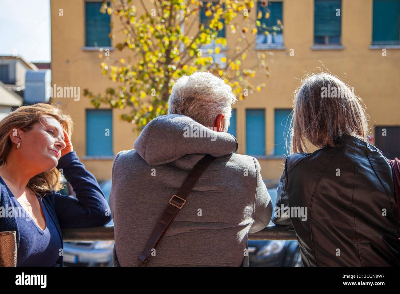 Three middle-aged commuters standing leaning on a railing and looking at a building while waiting for the bus Stock Photo