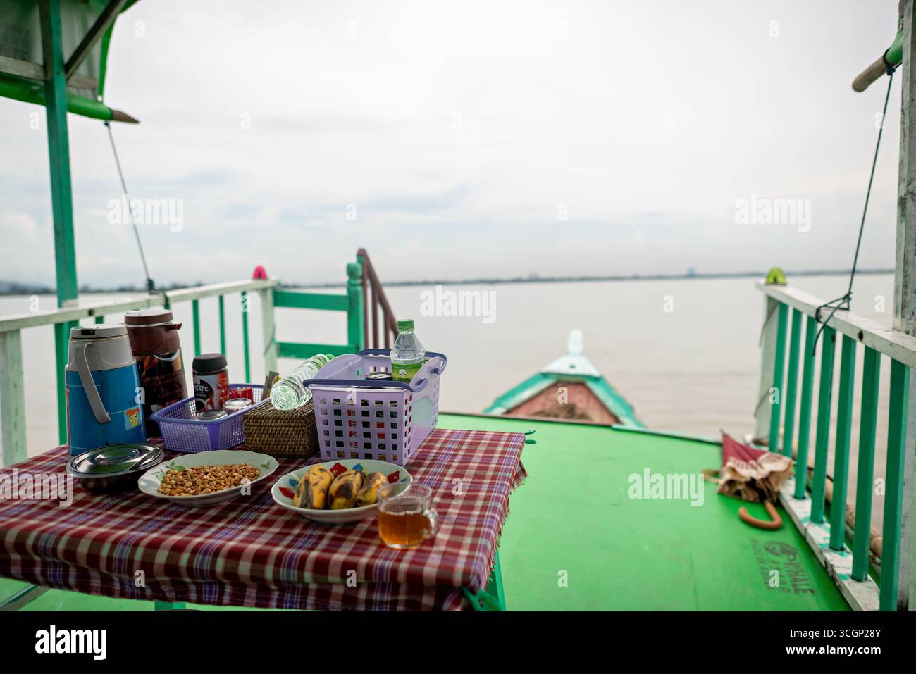 Ayeyarwaddy River Tourist Boat Snack Spread Mandalay Myanmar // MANDALAY, Myanmar — A snack spread, including peanuts, bananas, and tea, is laid out on a table aboard a tourist boat. The boat is cruising the Ayeyarwady River (also known as Irrawaddy River), Myanmar's longest and most important commercial waterway. River cruises are a popular way for tourists to travel between key cities like Mandalay and Bagan, offering scenic views and cultural immersion. The Ayeyarwady River is vital for transport, trade, and the livelihoods of many communities along its banks. Mandalay, located in the Manda Stock Photo