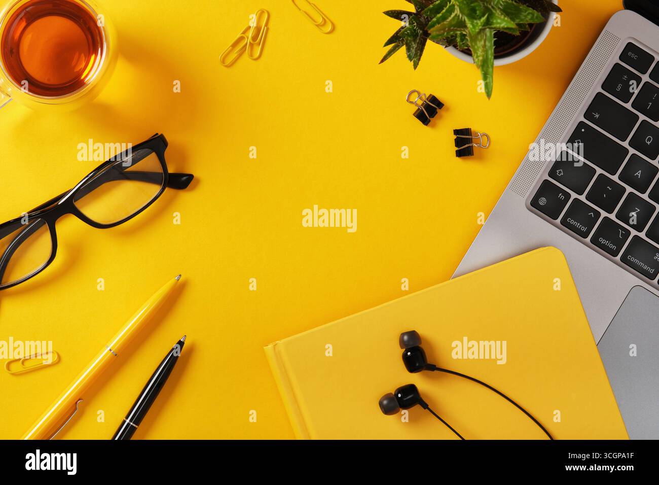 Yellow desk with laptop, notebook, glasses, pens, and earphones ...