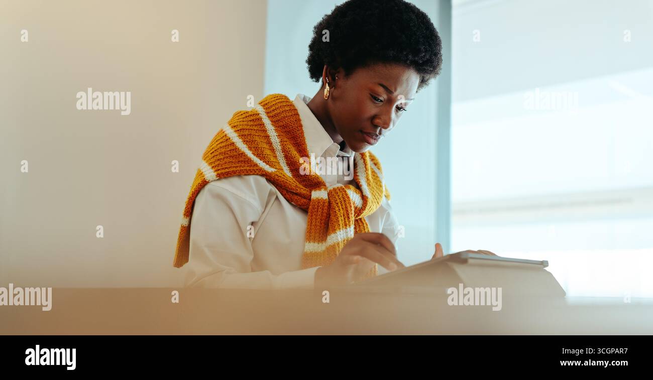 A focused woman engrossed in her work on a tablet, embodying concentration and productivity in a modern setting. Her thoughtful expression and relaxed Stock Photo