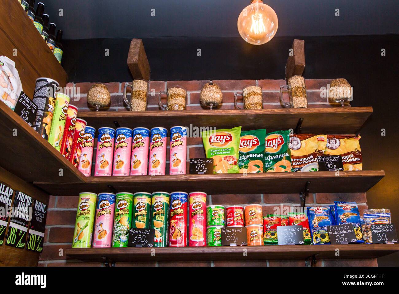 moskow russia, 25.04.2019 Snacks and beer bottles displayed on wooden shelves with a brick wall background, decorated with grain-filled mugs and glass Stock Photo