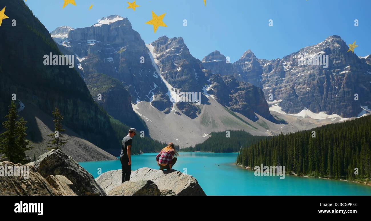 Watching couple on boulder overlooking turquoise lake, snow-capped peaks, star overlays, copy space Stock Photo