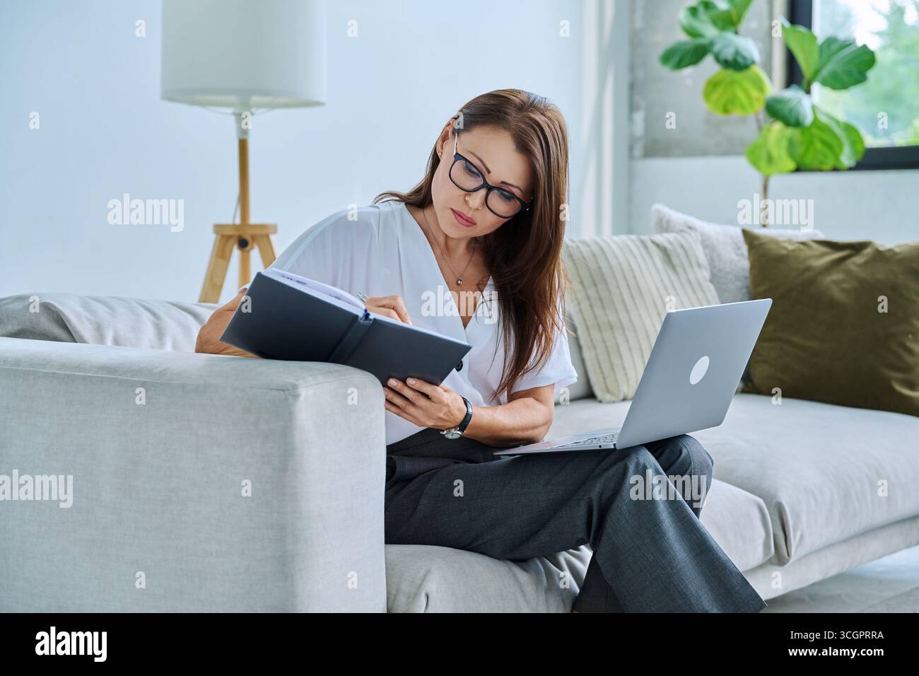 Middle aged serious woman working on c with laptop notepad Stock Photo
