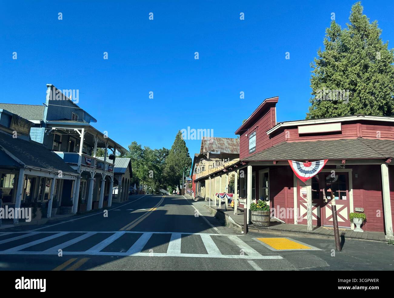 Street view of a small historic town with old wooden storefronts, rustic architecture, and patriotic bunting decoration under a clear blue sky. Stock Photo