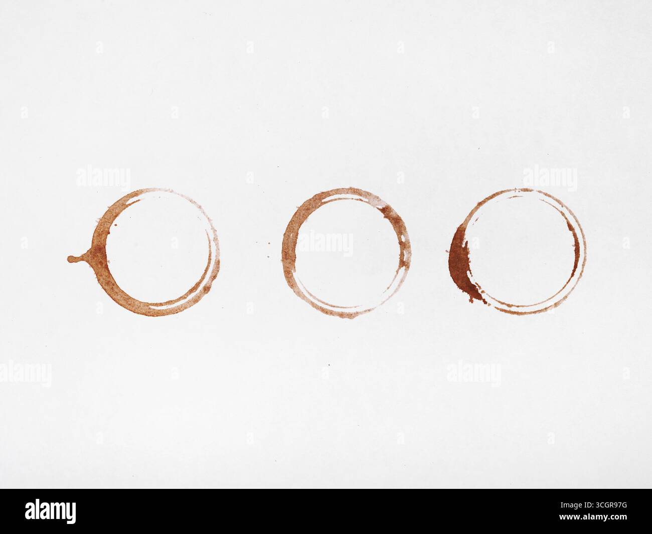 Three coffee rings and scattered droplets on a white background. Stock Photo