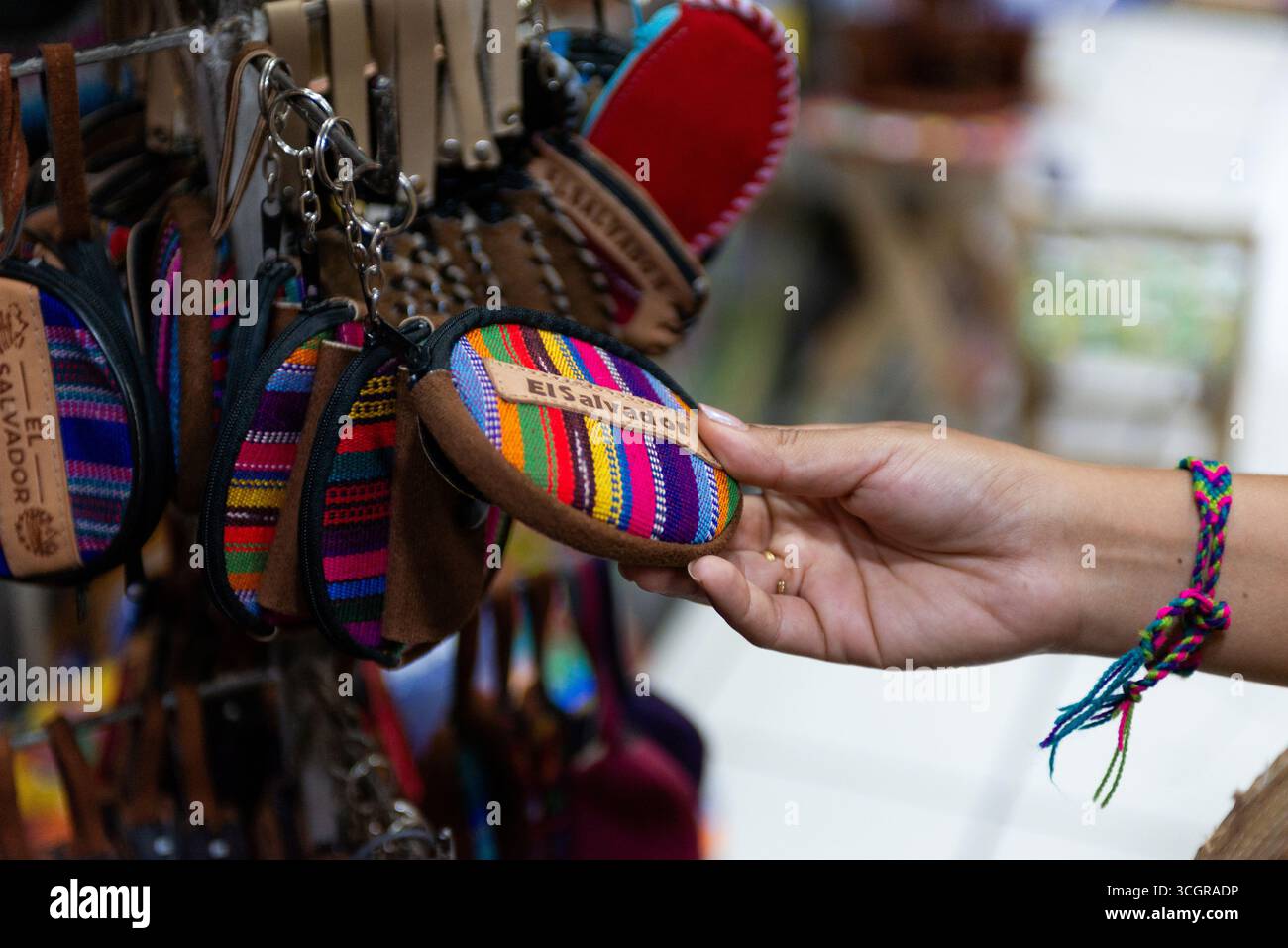 A hand chooses a small, brightly colored coin purse with text 'El Salvador' on it. Stock Photo