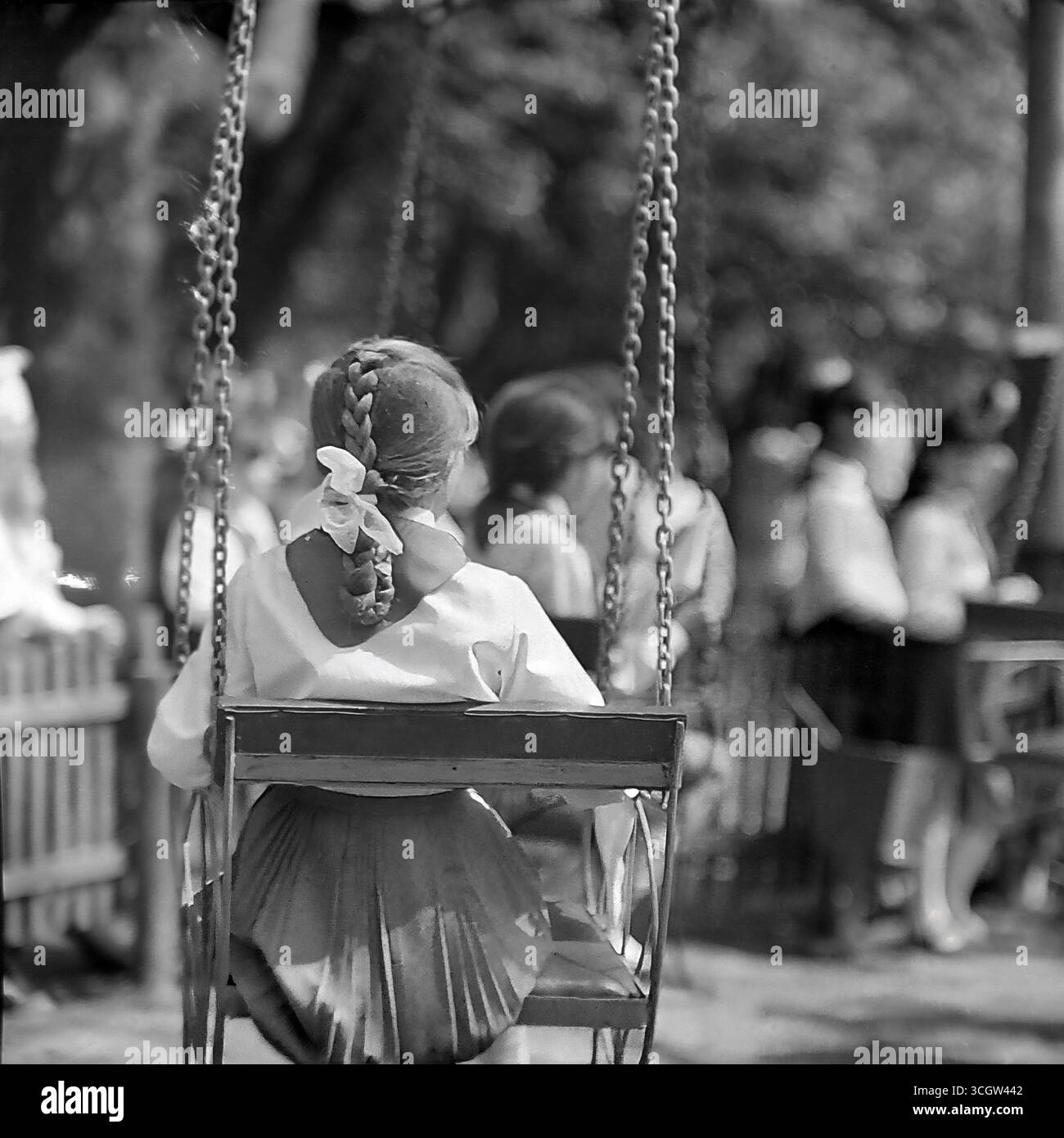 A nostalgic photo of a Soviet schoolgirl with a plait and a white bow, sitting on a swing in a park in Sloviansk, 1970, as an archetypal symbol of a happy and peaceful childhood in Donbas before the war Stock Photo